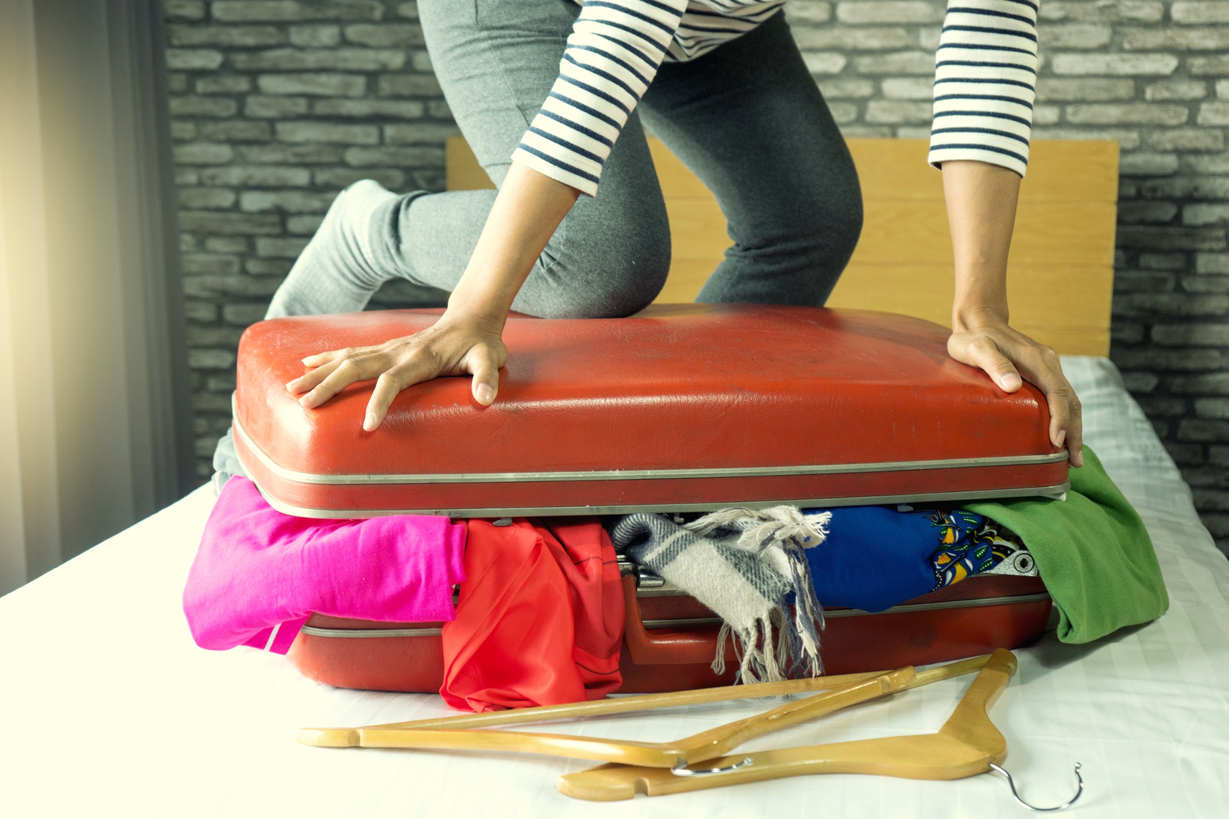 Women kneeling on top of luggage trying to close it