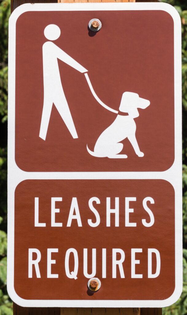 brown and white sign that says leashes required